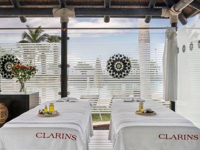 Buiten spa met twee massagetafels en uitzicht op de oceaan, versierd met bloemen en houten elementen.