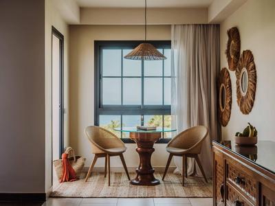 Gezellige zithoek met twee stoelen, een ronde tafel en een raam met uitzicht op de zee in een hotelkamer.