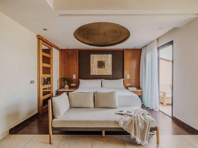 Knusse hotelkamer met een bed, bank, houten accenten, kunstwerk en natuurlijk licht via een raam.