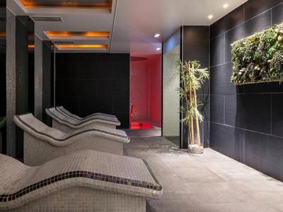 Moderne spa-lounge met ligstoelen en planten aan donkere betegelde muren.