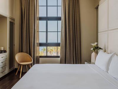 Gezellige hotelkamer met groot bed, bruine gordijnen, fauteuil en raam met uitzicht op buiten.