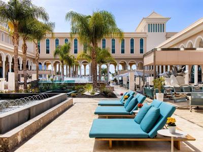 Luxe hotelzwembad met palmbomen, ligbedden met blauwe kussens en elegante architectuur.