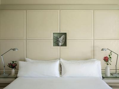 Hotelkamer met groot bed, witte kussens, twee bedlampjes en kleine bloemenvaasjes.