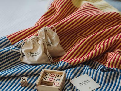 Gezellig bed met gestreepte lakens, dobbelspel en klein zakje met trekkoord op wit matras.