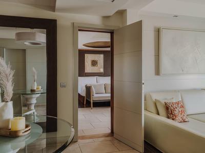 Moderne hotelsuite met neutrale kleuren, banken, glazen tafel en decoratieve accenten.