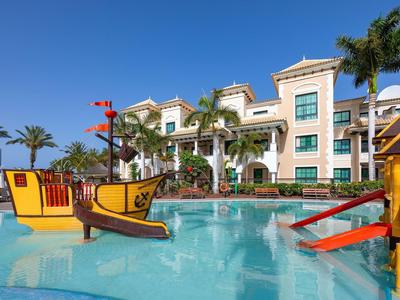 Hotelzwembad met piraten-speelgedeelte bij een heldere blauwe lucht en palmbomen.