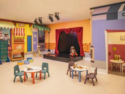 Kleurrijke speelkamer voor kinderen met podium, kleine tafels en stoelen voor activiteiten.