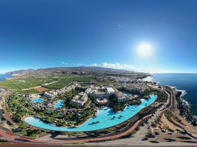 Kustresort met groot zwembad, omgeven door groen, zee en heldere zonnige lucht.