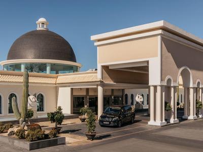 Hotel ingang met een koepelvormig dak, beige muren, bogen en een zwarte auto buiten geparkeerd.