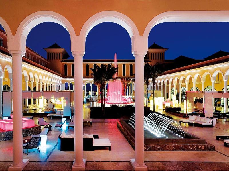 Buitenhouten terrasrestaurant met tafels en stoelen aan zee bij zonsondergang, zeilboten in het water.
