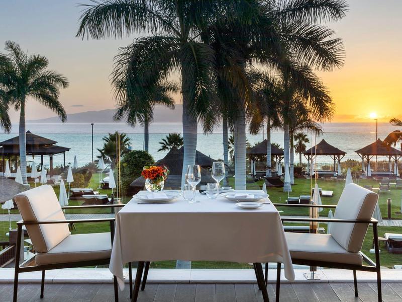 Tafel voor twee op een terras met palmbomen en zonsondergang boven de zee op de achtergrond.