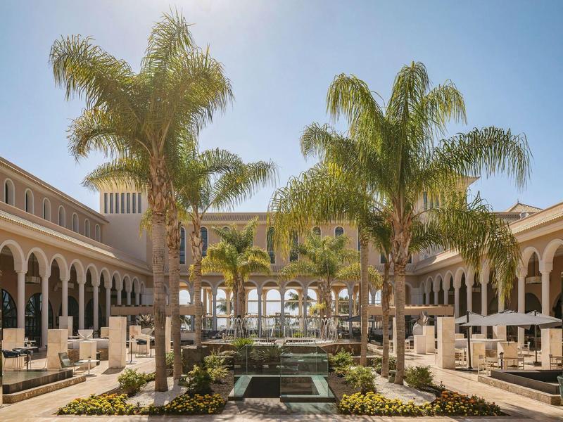 Binnenplaats met palmbomen, bogen en zitplaatsen bij een zonnig luxe resort.