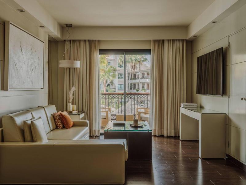 Gezellige hotel lounge met bank, salontafel, tv en balkonzicht.