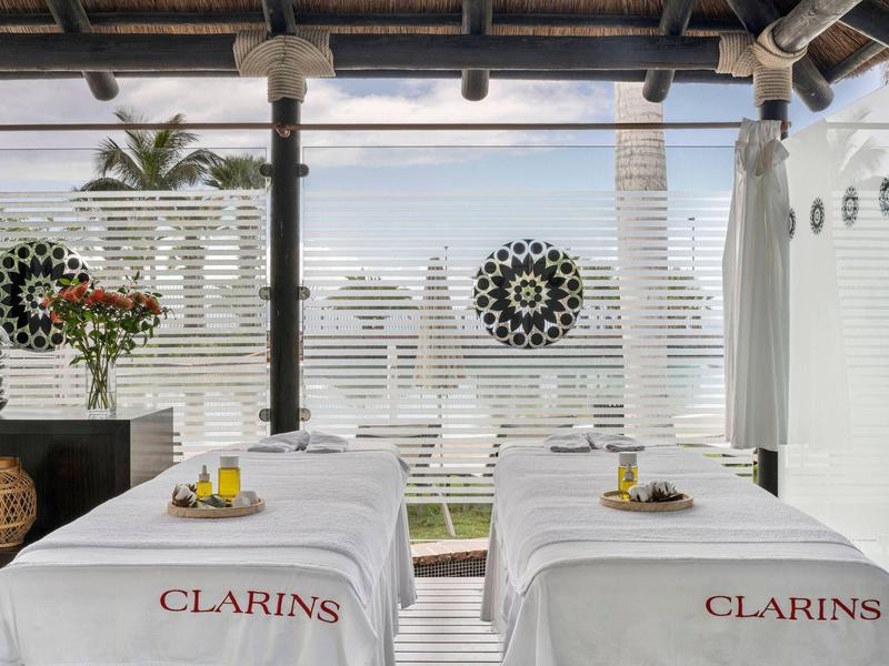 Buiten spa met twee massagetafels en uitzicht op de oceaan, versierd met bloemen en houten elementen.