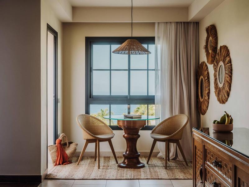Gezellige zithoek met twee stoelen, een ronde tafel en een raam met uitzicht op de zee in een hotelkamer.