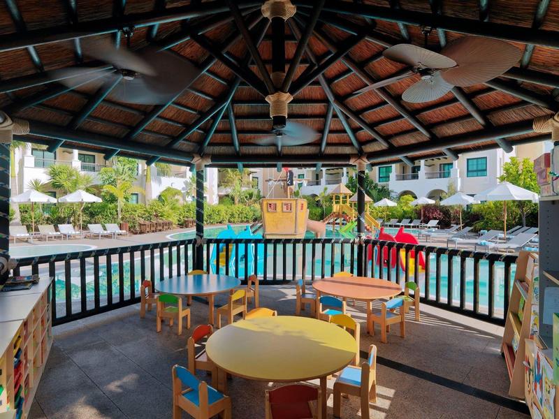 Overdekt terras met kleurrijke tafels en stoelen met uitzicht op zwembad en lounge gebied.