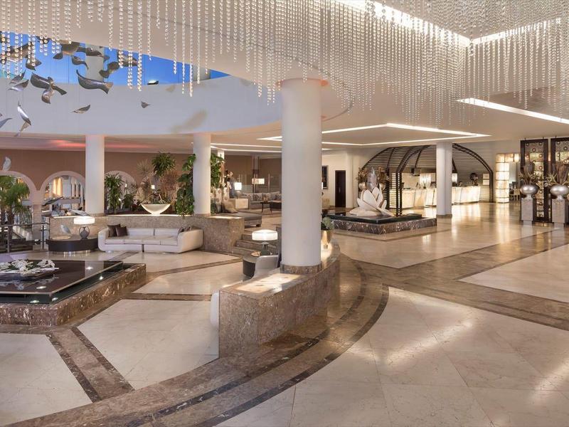 Ruime hotel lobby met moderne zitplekken, waterpartijen en elegante verlichting.