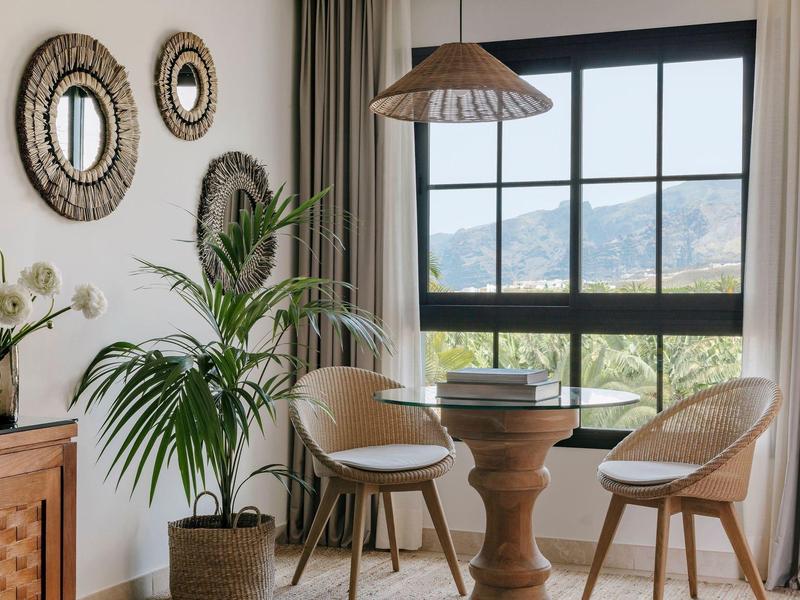 Gezellige zithoek bij raam met uitzicht op bergen, met twee stoelen, houten tafel en kamerplanten.