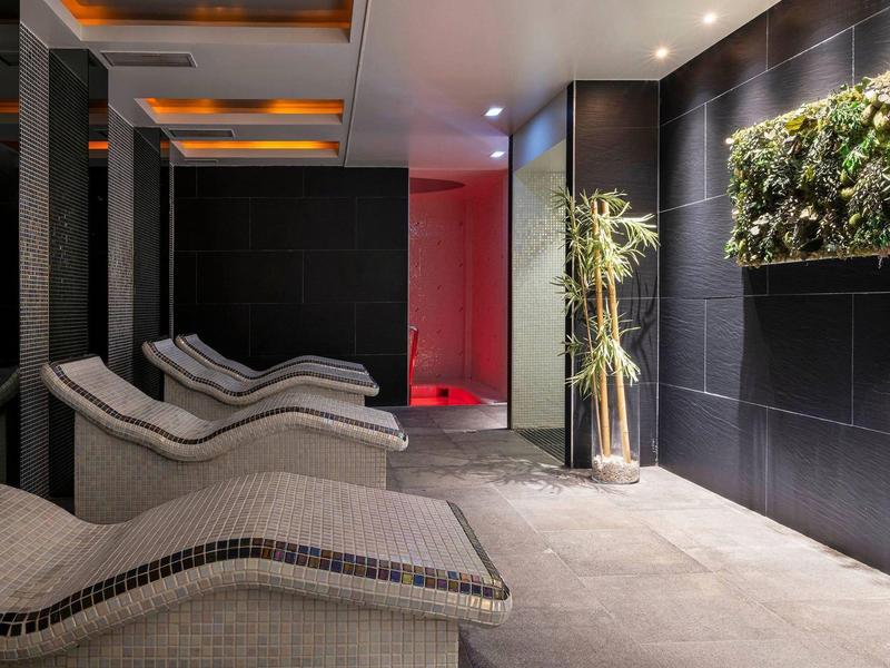 Moderne spa-lounge met ligstoelen en planten aan donkere betegelde muren.