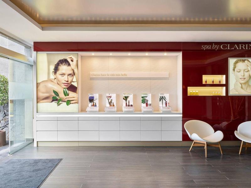 Moderne hotel lobby met witte stoelen, vitrines en promotieposters aan bordeauxrode muur.