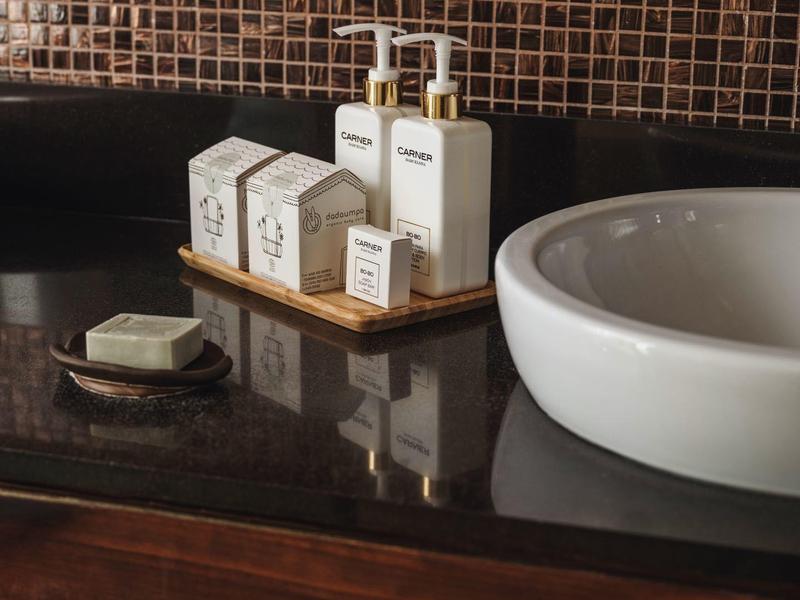 Elegante badkamer toonbank met toiletartikelen, zeep en witte wastafel onder mozaïektegels.