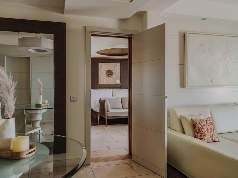 Moderne hotelsuite met neutrale kleuren, banken, glazen tafel en decoratieve accenten.