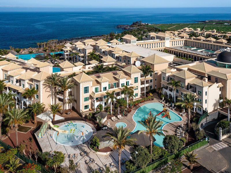 Resort met meerdere zwembaden, palmbomen en zeezicht onder een heldere blauwe lucht.