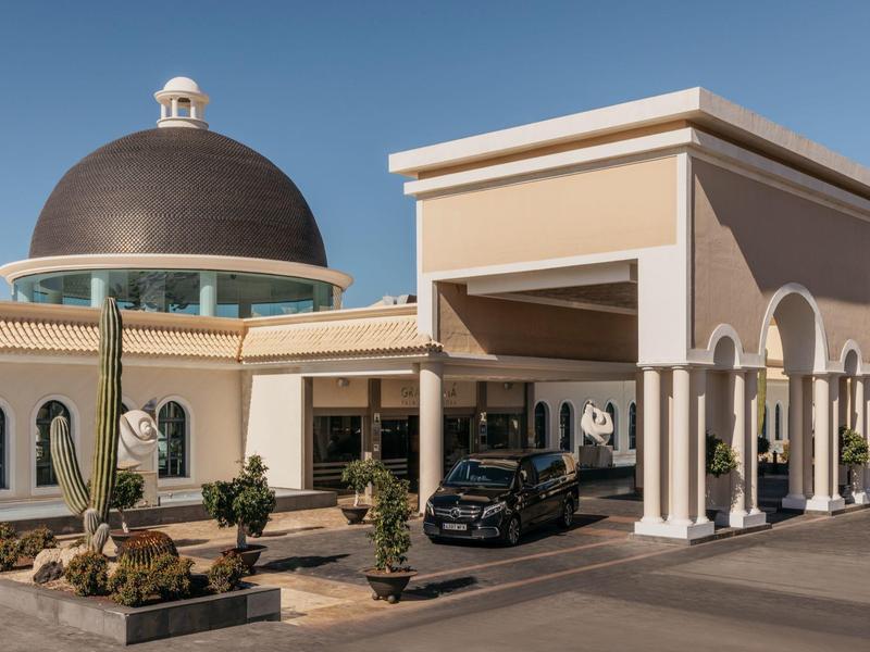 Hotel ingang met een koepelvormig dak, beige muren, bogen en een zwarte auto buiten geparkeerd.
