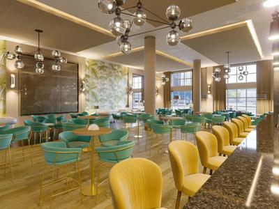 Moderní restaurace s žlutými a zelenými židlemi a geometrickými svítidly.