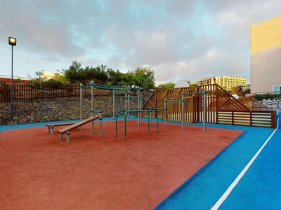 A playground with climbing frame and slide next to a blue running track at a hotel.