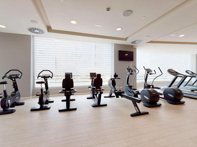 Modern gym with various exercise machines and large windows.