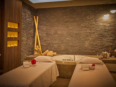 A cozy spa room with two treatment beds, warm lighting, and a relaxing atmosphere.