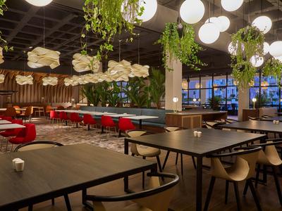 Modern hotel restaurant with stylish tables, seating, and hanging plants under soft lighting.