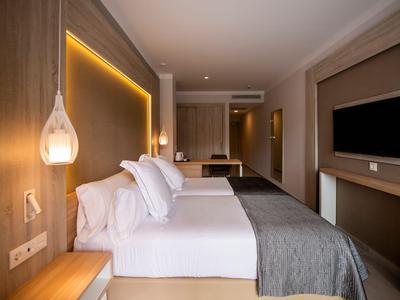 Modern hotel room with large bed, gray blanket, and TV on the wall.