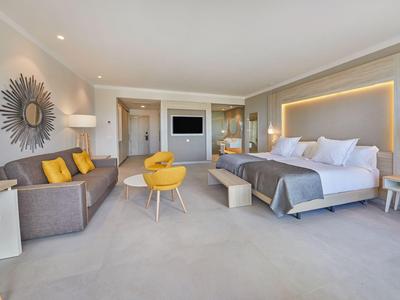 Modern hotel room with large bed, sofa, and yellow accents.