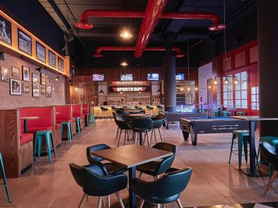 Modern hotel bar area with seating and game table under warm lighting.