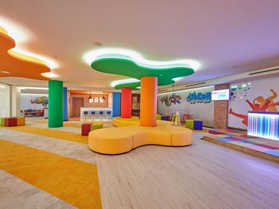 Modern hotel lobby with colorful columns, yellow seating, and light wood flooring.