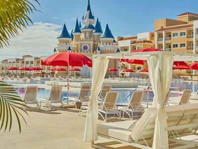Leisure area with pool, sun loungers, and a castle-like hotel building in the background.