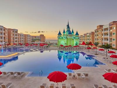Large pool area with red umbrellas and castle attraction in the background at sunset.