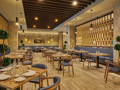 Modern hotel restaurant with wooden floors, tables and chairs, and warm lighting.