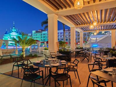 Open hotel restaurant area with evening lighting and view of illuminated buildings.