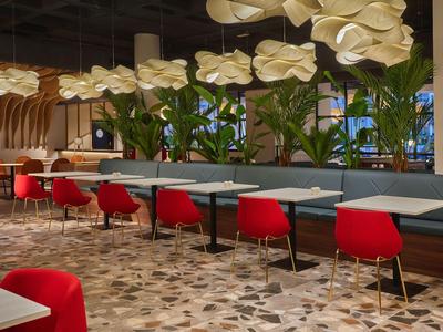 Modern hotel restaurant area with red chairs, white tables, and hanging lamps.