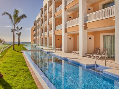 Modern hotel with balcony rooms, pool, and sea view at sunset.