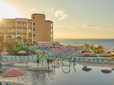 Hotel s bazénem a slunečníky u moře při západu slunce.