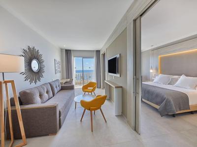 Moderní hotelový pokoj s obývacím prostorem, balkonem a přilehlou ložnicí s manželskou postelí.