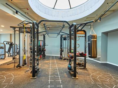 Moderní posilovna se stanicí na cvičení a boxovacím pytlem pod světlým kruhovým oknem.