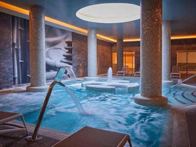 Moderní vnitřní bazén s kulatými sloupy, vodní fontánou a teplou atmosférou.