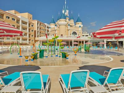 Pohled na vodní hřiště s lehátky a budovou hotelu v pozadí.