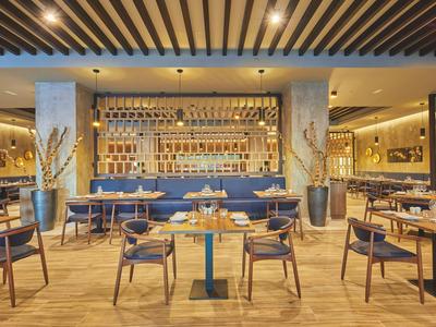 Moderně zařízená hotelová restaurace s dřevěnými stoly, modrými lavicemi a stylovým osvětlením.