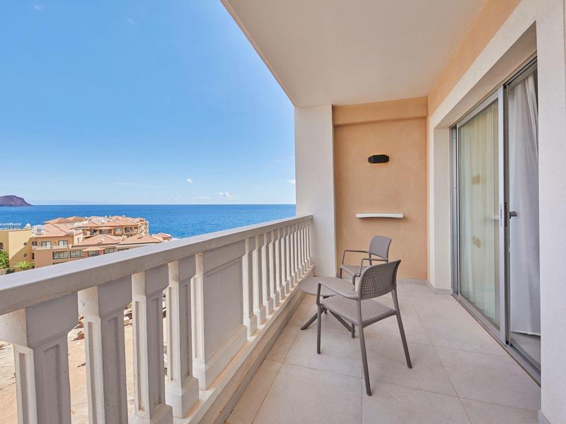 Balkon se židlí a výhledem na moře, slunečný den a jasná obloha.